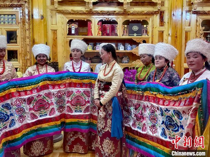 圖為女性展示村民自發(fā)繡制的“百米五彩哈達”?！±钣穹?攝